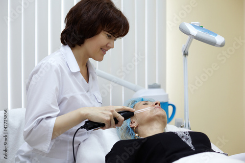 Photo: The employee of beauty salon processes face skin of the patient The employee of beauty salon processes face skin of the patient