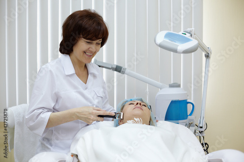Photo: Smiling beautician in beauty salon processes face skin Smiling beautician in beauty salon processes face skin