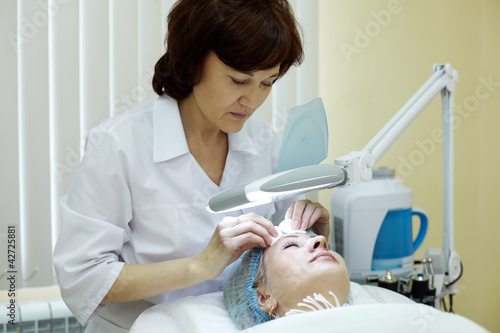 Photo: Beautician in beauty salon cleans facial skin of woman. Beautician in beauty salon cleans facial skin of woman.