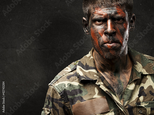 Photo: young soldier with camouflage paint looking very serious against young soldier with camouflage paint looking very serious against
