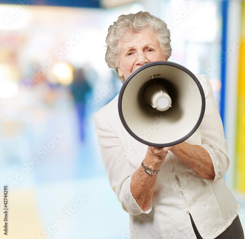 Photo: portrait of senior woman screaming with megaphone at crowded pla portrait of senior woman screaming with megaphone at crowded pla