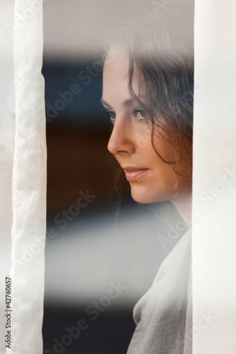 Photo: Sad beautiful woman looking through the window Sad beautiful woman looking through the window