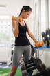 Young latina woman taking weights from rack in fitness club
