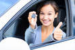 Happy girl in a car showing a key and thumb up gesture