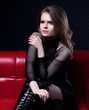 Foto: Luxurious pretty dreamy woman in black dresson red sofa sitting Luxurious pretty dreamy woman in black dresson red sofa sitting