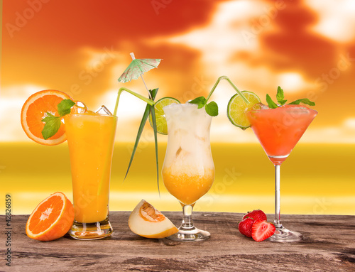 Photo: Summer cocktails in sunset with blur beach on background Summer cocktails in sunset with blur beach on background