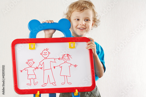 Photo: Little smiling cute boy shows his family painted on a whiteboard Little smiling cute boy shows his family painted on a whiteboard