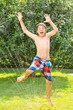 Foto: Endlich Sommer - Junge springt durch Wasserstrahl, Rasensprenger Endlich Sommer - Junge springt durch Wasserstrahl, Rasensprenger