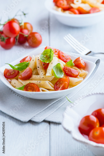 Photo: Pasta salad with fresh cherry tomatoes on kitchen table Pasta salad with fresh cherry tomatoes on kitchen table
