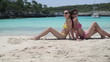 Two female friends sunbathing on the beach, tracking shot