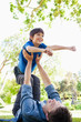 A boy with his arms out smiling as his dad holds him up