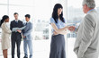 Two business people shaking hands and three others looking at some files