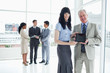 Two smiling business people standing upright showing a tablet computer