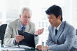 Photo: Mature businessman giving serious explanations about information on the clipboard to an employee Mature businessman giving serious explanations about information on the clipboard to an employee