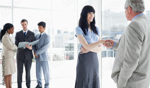 Photo: Two business people shaking hands and three others looking at some files Two business people shaking hands and three others looking at some files