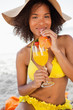 Photo: Young smiling woman drinking a fruit cocktail while wearing a yellow swimsuit Young smiling woman drinking a fruit cocktail while wearing a yellow swimsuit