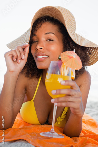 Photo: Young attractive woman holding her hat brim while lying down with a cocktail Young attractive woman holding her hat brim while lying down with a cocktail