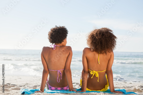 Photo: Young attractive women sitting on beach towels Young attractive women sitting on beach towels
