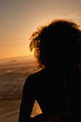 Rear view of a young attractive woman standing on the beach at sunset