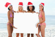 Four friends present a blank poster while wearing Santa hats