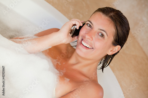 Photo: Smiling woman with her mobile phone in the tub Smiling woman with her mobile phone in the tub