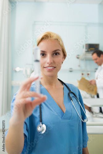 Photo: Blonde nurse holding a syringe while looking at camera Blonde nurse holding a syringe while looking at camera