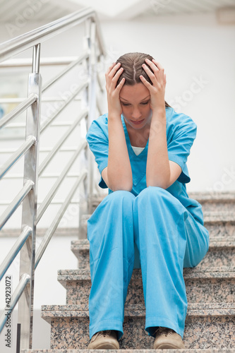 Photo: Nurse holding her head with her two hands in stairs Nurse holding her head with her two hands in stairs