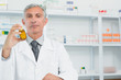 Serious pharmacist holding a bottle full of pills with one hand