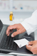 Pharmacist holding a prescription while typing on a computer