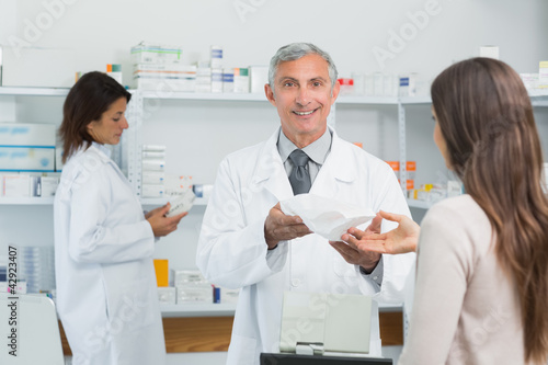Photo: Pharmacist in a drugstore giving a bag of pills to a female client Pharmacist in a drugstore giving a bag of pills to a female client