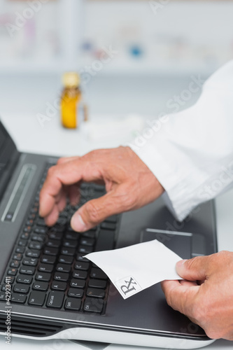 Photo: Pharmacist holding a prescription while typing on a computer Pharmacist holding a prescription while typing on a computer