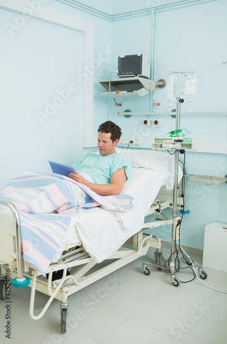 Photo: Focus male patient holding a tactile tablet while lying on a bed Focus male patient holding a tactile tablet while lying on a bed