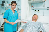 Photo: Smiling nurse touching the shoulder of a smiling patient lying on a bed while holding a paper Smiling nurse touching the shoulder of a smiling patient lying on a bed while holding a paper