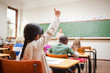 Back view of young student raising hand