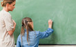 Photo : Teacher supervising pupil writing on blackboard Teacher supervising pupil writing on blackboard