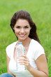 Jeune femme brune souriante buvant de l'eau dans un champ