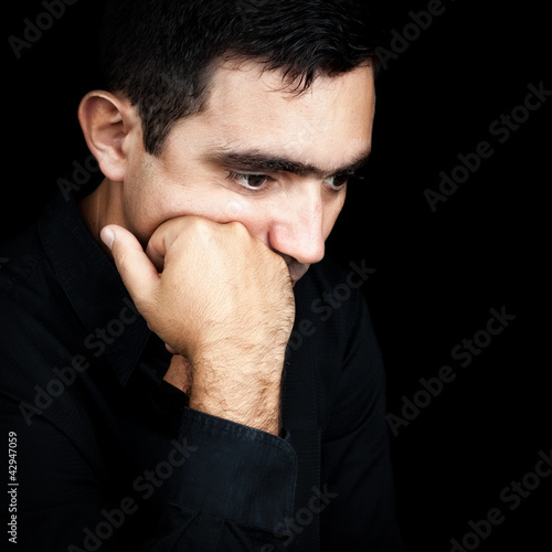Photo: Hispanic man thinking with a fist on his chin isolated on black Hispanic man thinking with a fist on his chin isolated on black