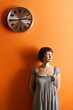 Young woman standing below a large clock on an orange wall