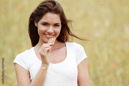 Photo: Jeune femme mangeant un gateau aux céréales dans un champ de blé Jeune femme mangeant un gateau aux céréales dans un champ de blé