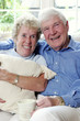 An old man sitting on the couch with his arm around his wife