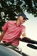An old man with cap and sunglasses standing beside his roofless car
