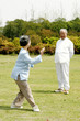An old man watching his wife practicing tai chi in the park