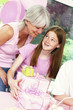 A girl holding her birthday presents as her mother watching