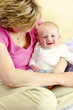 A baby boy smiling happily sitting on his mother's lap