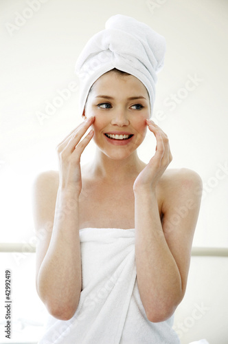 Photo: A woman with her hair and body wrapped up in towel smiling while applying under eye cream A woman with her hair and body wrapped up in towel smiling while applying under eye cream