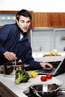 Man cooking, using laptop and talking on the hand phone at the same time