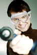 Man with goggles pointing a drill at the camera