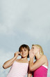 Woman whispering to her friend who is talking on the mobile phone