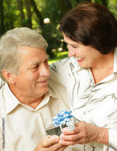Photo: Mature happy smiling couple embracing in park with gift Mature happy smiling couple embracing in park with gift