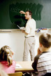 Photo : Teacher writing on the blackboard with children paying attention Teacher writing on the blackboard with children paying attention